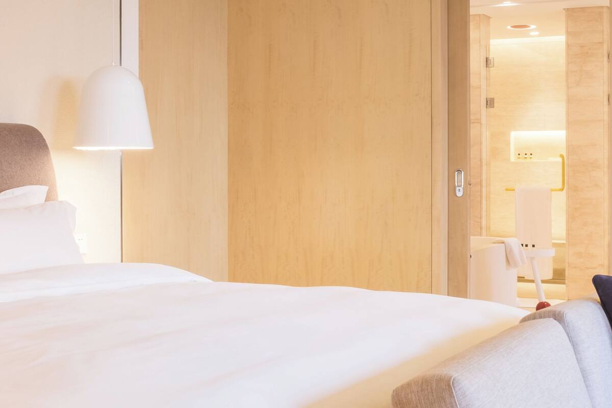 Una habitación de hotel con una cama grande, una mesita de noche, una lámpara y una puerta que da a un baño.