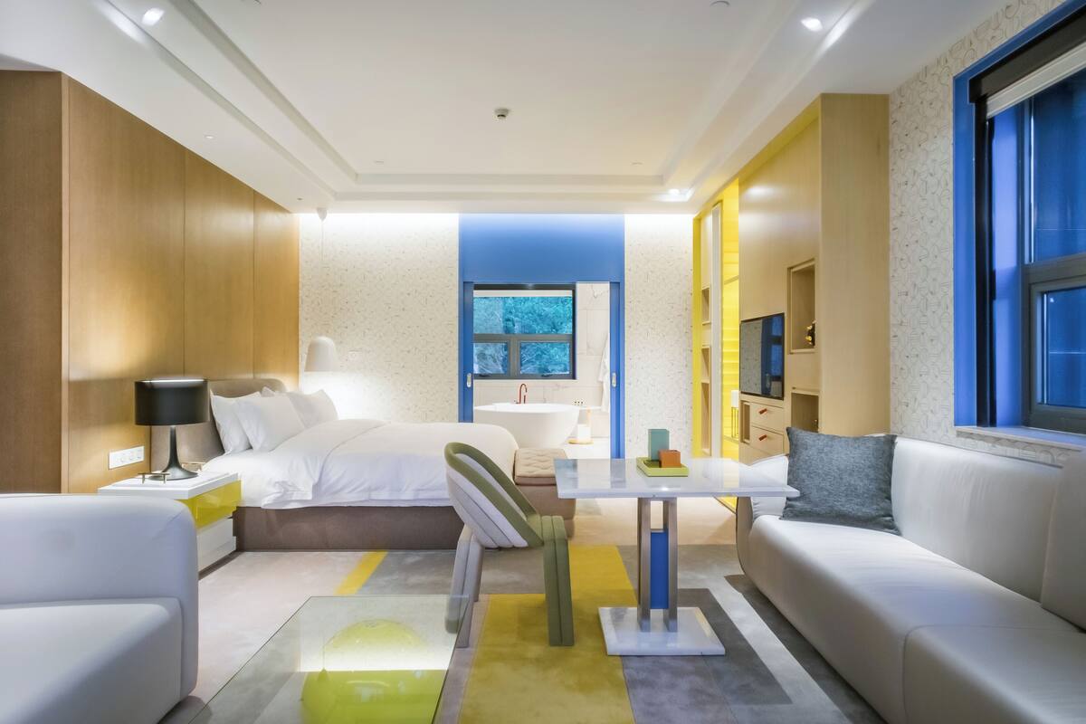 Una habitación de hotel moderna con cama, sofá, mesa de comedor y televisor.
