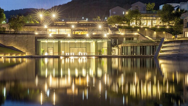 Ein modernes Gebäude mit einem spiegelnden Pool davor, mit einer Glasfassade und mehreren Lichtquellen.