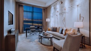 A modern hotel room with a large window offering a city view, a sofa with cushions, a coffee table, and a desk with a lamp. - Wanda Realm Huangshi (Huangshi)
