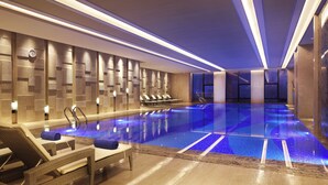 A modern indoor swimming pool with lounge chairs and a sunbed, surrounded by a tiled wall and a ceiling with linear lighting. - Wanda Realm Huangshi (Huangshi)