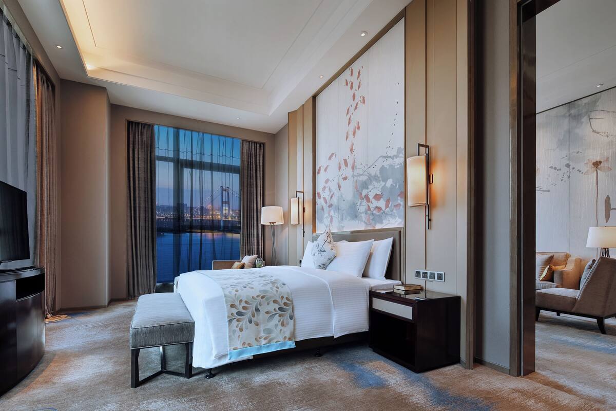 Ein modernes Hotelzimmer mit einem großen Bett, einem Schreibtisch, einem Stuhl und einem Fernseher.