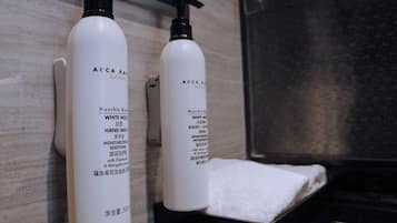 Two bottles of Acca Kawa body lotion and a white towel on a black surface.