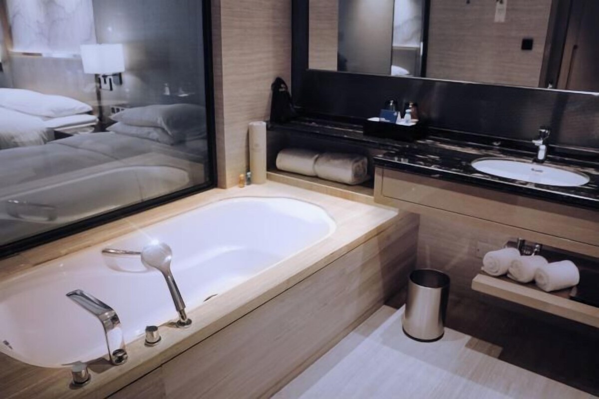 A modern bathroom with a large bathtub, a sink, and a mirror. There are towels and toiletries on the counter.