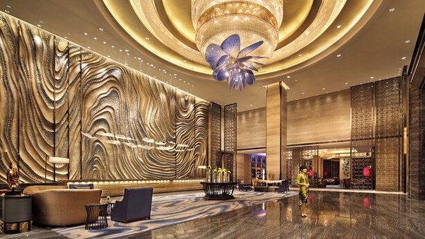 A spacious lobby with a large, ornate chandelier, a seating area with modern furniture, and a decorative wall with a wave pattern. - Wanda Realm Huangshi (Huangshi)