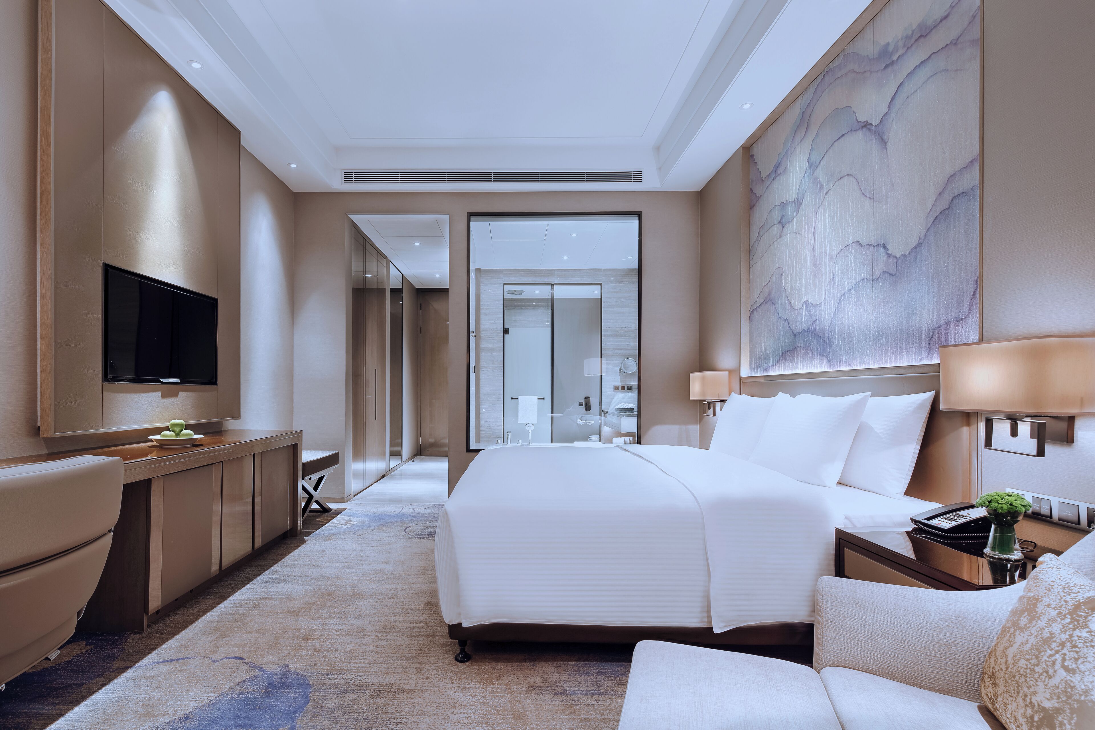 Una habitación de hotel moderna con una cama grande, un televisor de pantalla plana, un escritorio con lámpara y un cuadro abstracto de gran tamaño en la pared.