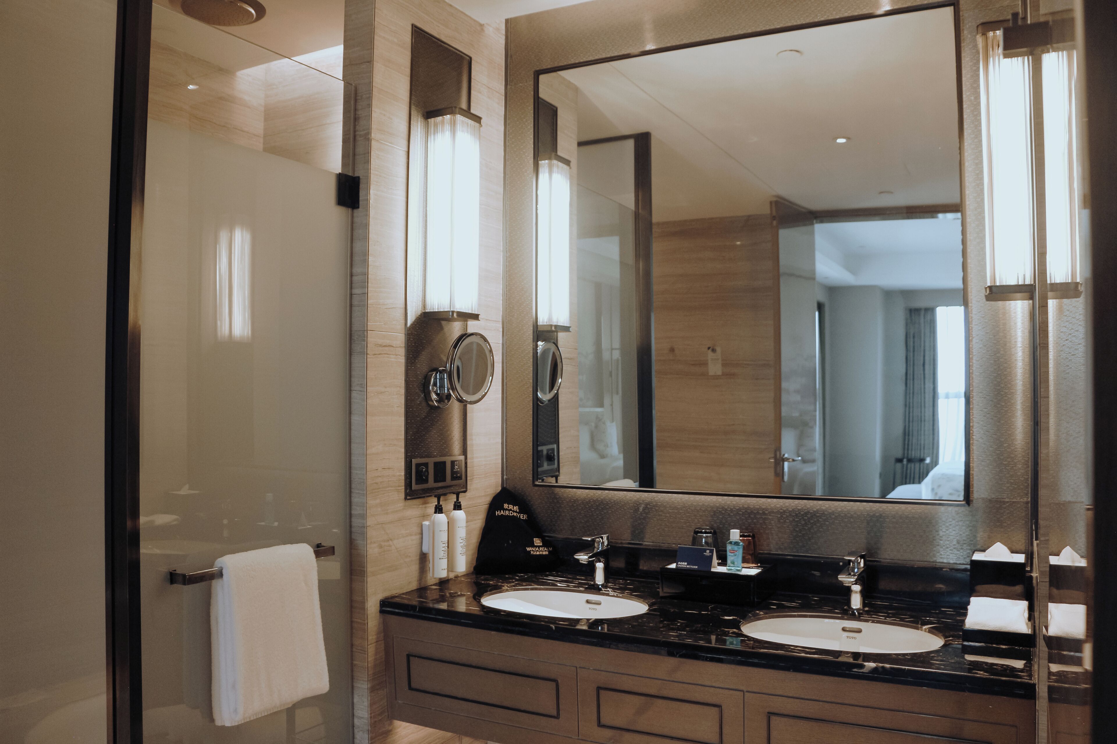 A modern bathroom with a large mirror, two sinks, and a glass shower enclosure.