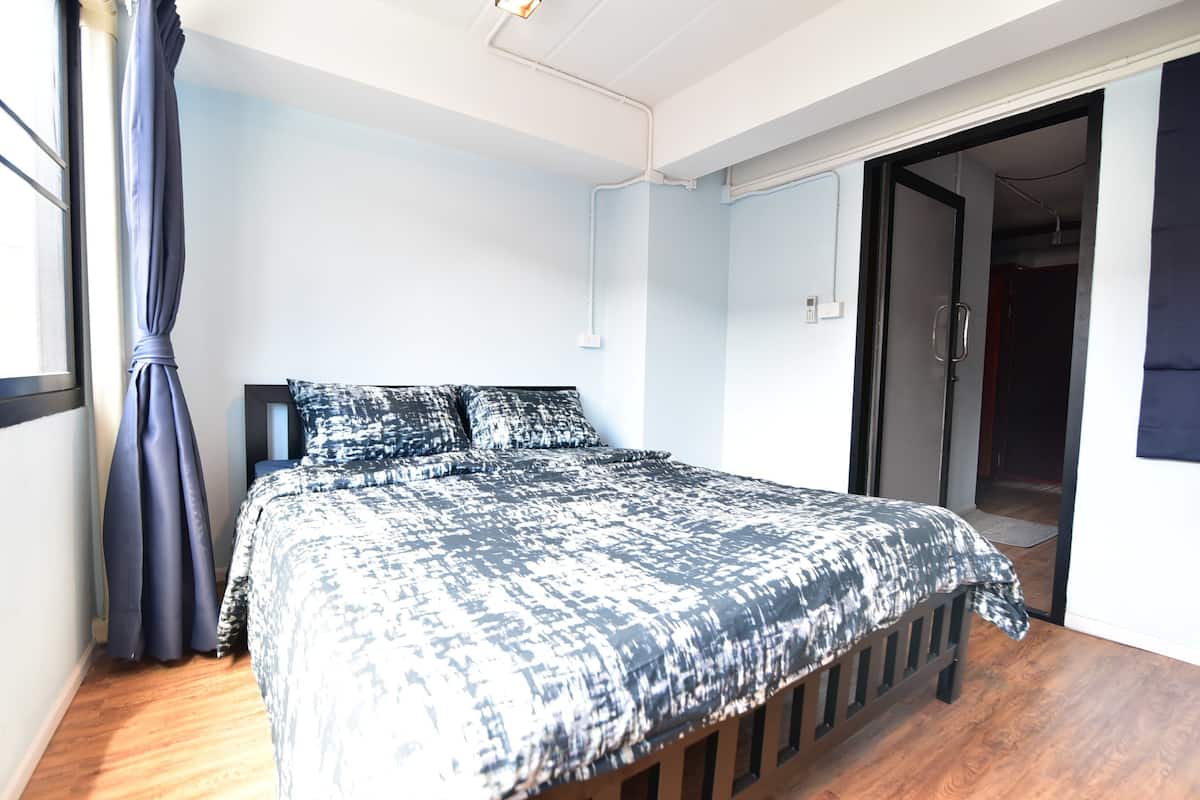 A bedroom with a bed, a window with curtains, and a door leading to another room.