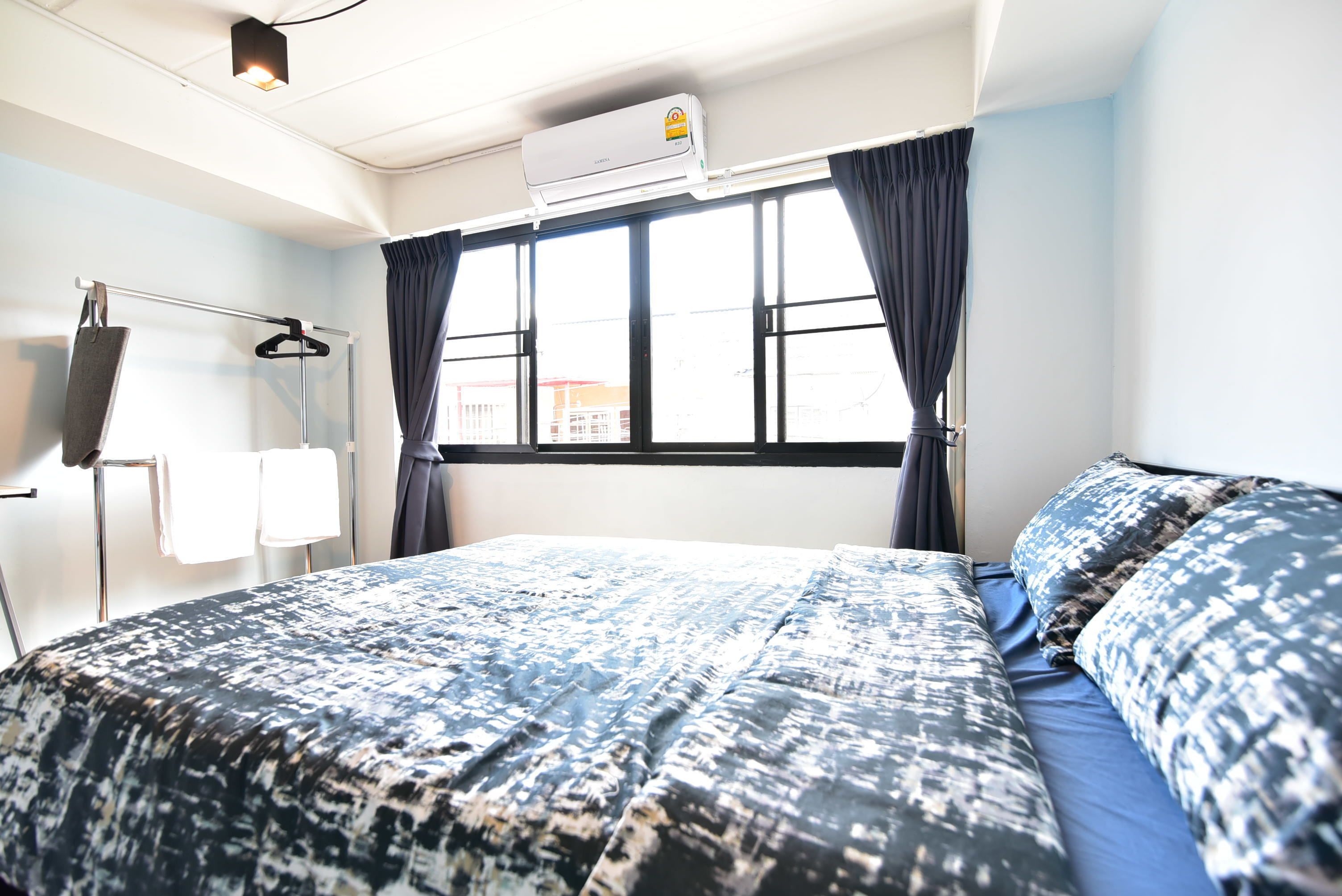 A hotel room with a bed, a window with curtains, an air conditioning unit, and a towel rack with towels.