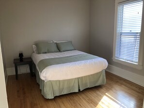 Ein Schlafzimmer mit einem Bett, einem Nachttisch, einem Fenster mit Jalousien und Holzboden.