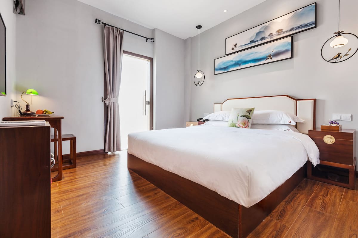 Une chambre moderne avec un plancher en bois, un grand lit recouvert de draps blancs, une table de chevet avec une horloge et une lampe fixée au mur.