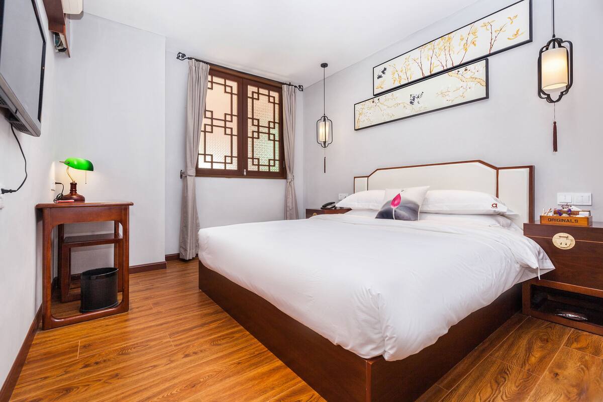 Une chambre à coucher bien rangée, avec un lit en bois, une table de chevet avec une lampe, une commode et un téléviseur fixé au mur.