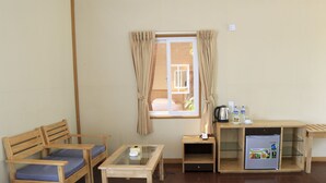 A room with a wooden sofa, a glass-top table, a small refrigerator, and a window with curtains. - Moe Yun Gyi Wetlands Resort (Bago)