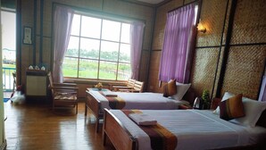 A room with two beds, wooden benches, a small table, and a view of a green landscape through large windows. - Moe Yun Gyi Wetlands Resort (Bago)