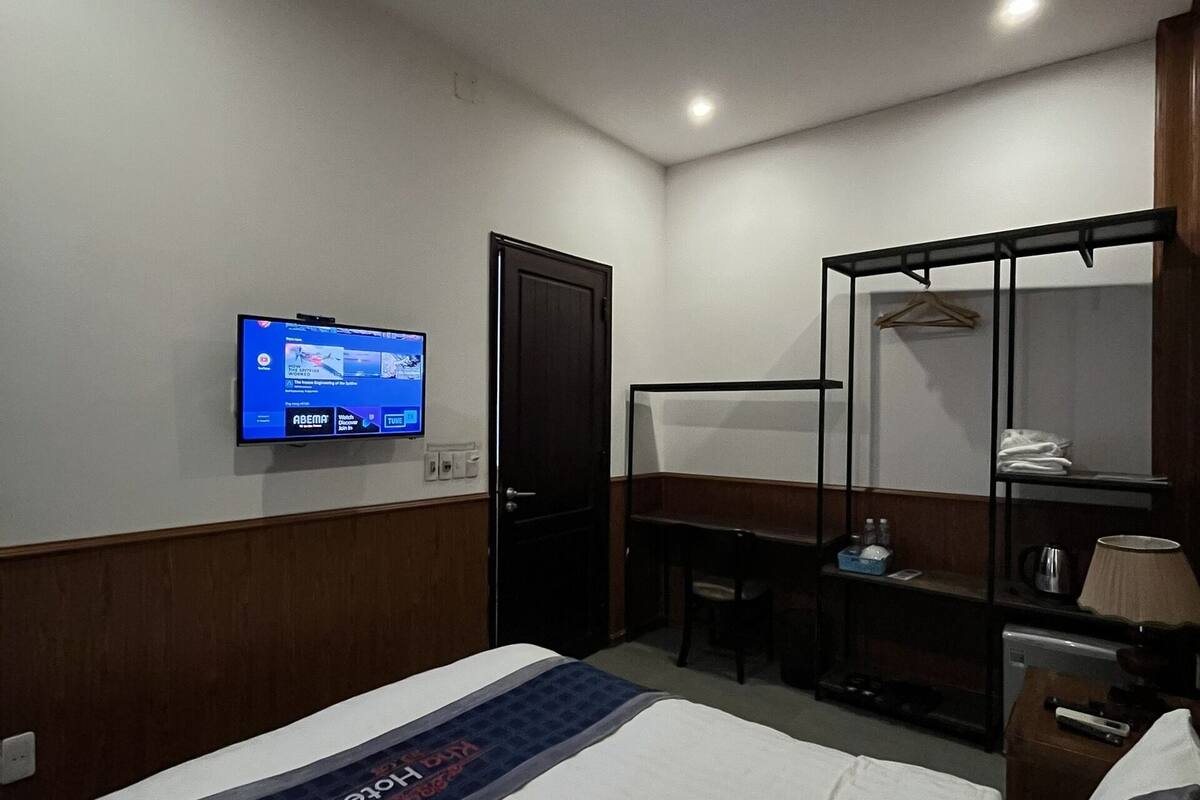 A hotel room with a bed, a desk, a chair, a TV mounted on the wall, and a wardrobe.