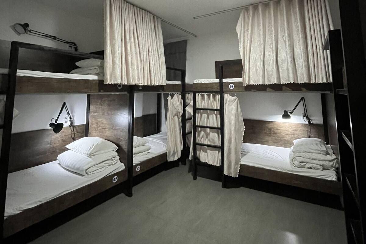 A dormitory room with bunk beds, each with a bedside lamp and a small shelf.