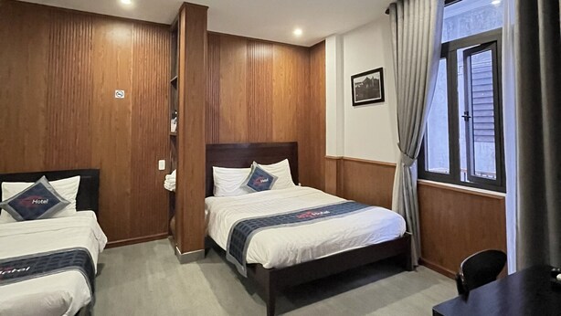 A hotel room with two beds, wooden paneling, a desk, and a window with curtains. - Kha Hotel - Hostel (Hue)