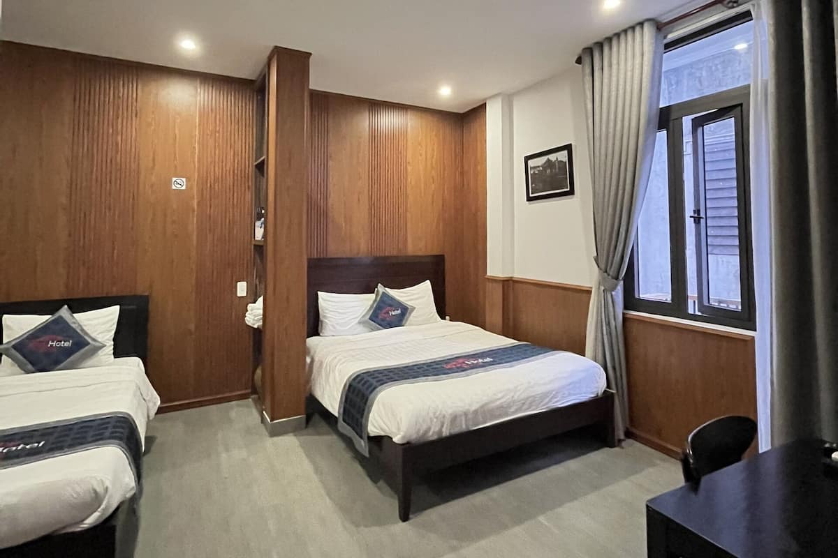 A hotel room with two beds, wooden paneling, a desk, and a window with curtains.