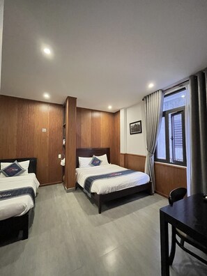 A hotel room with two beds, wooden paneling, a desk, and a window with curtains.