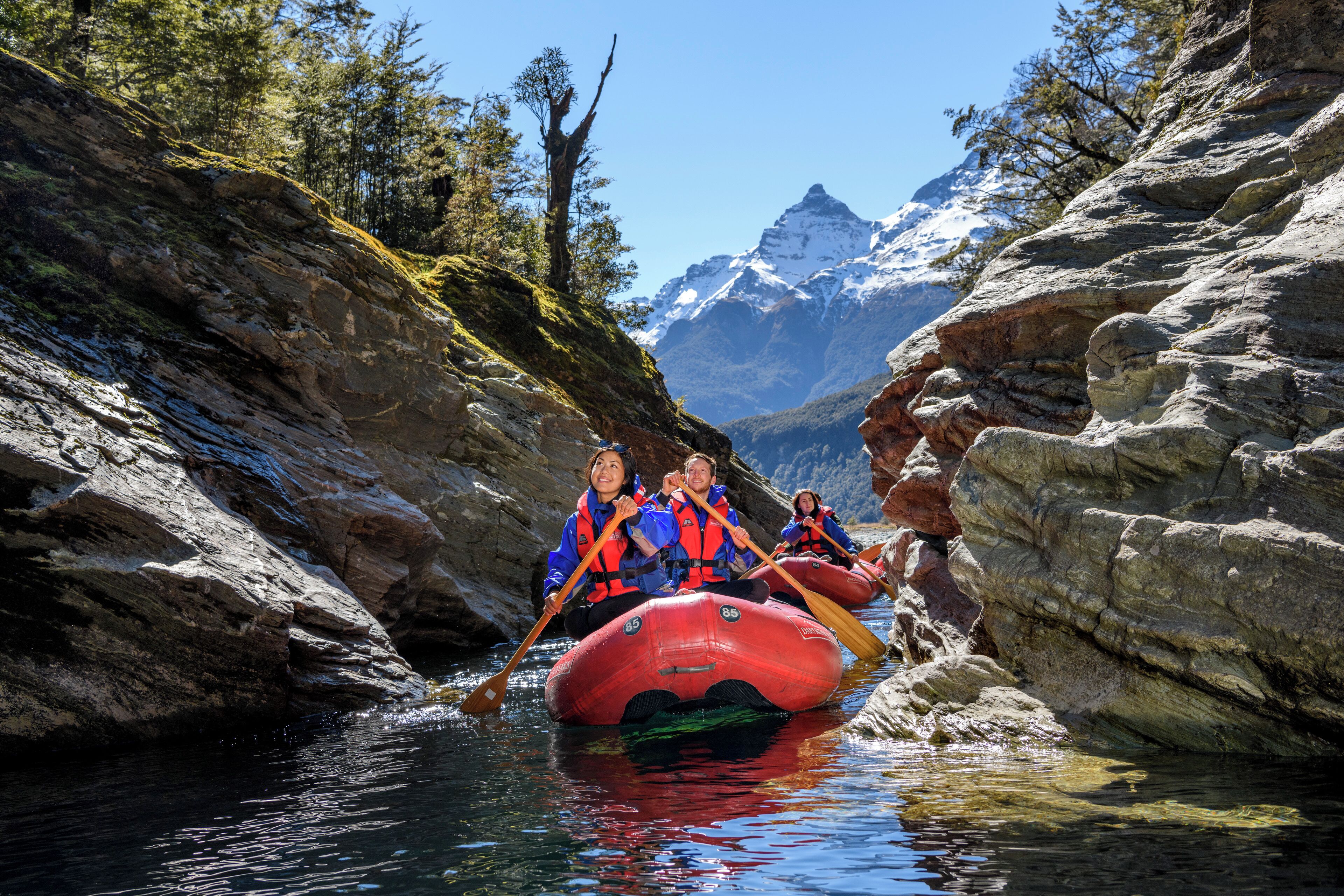 A group of people in a red raft navigating a narrow, rocky waterway surrounded by mountains.