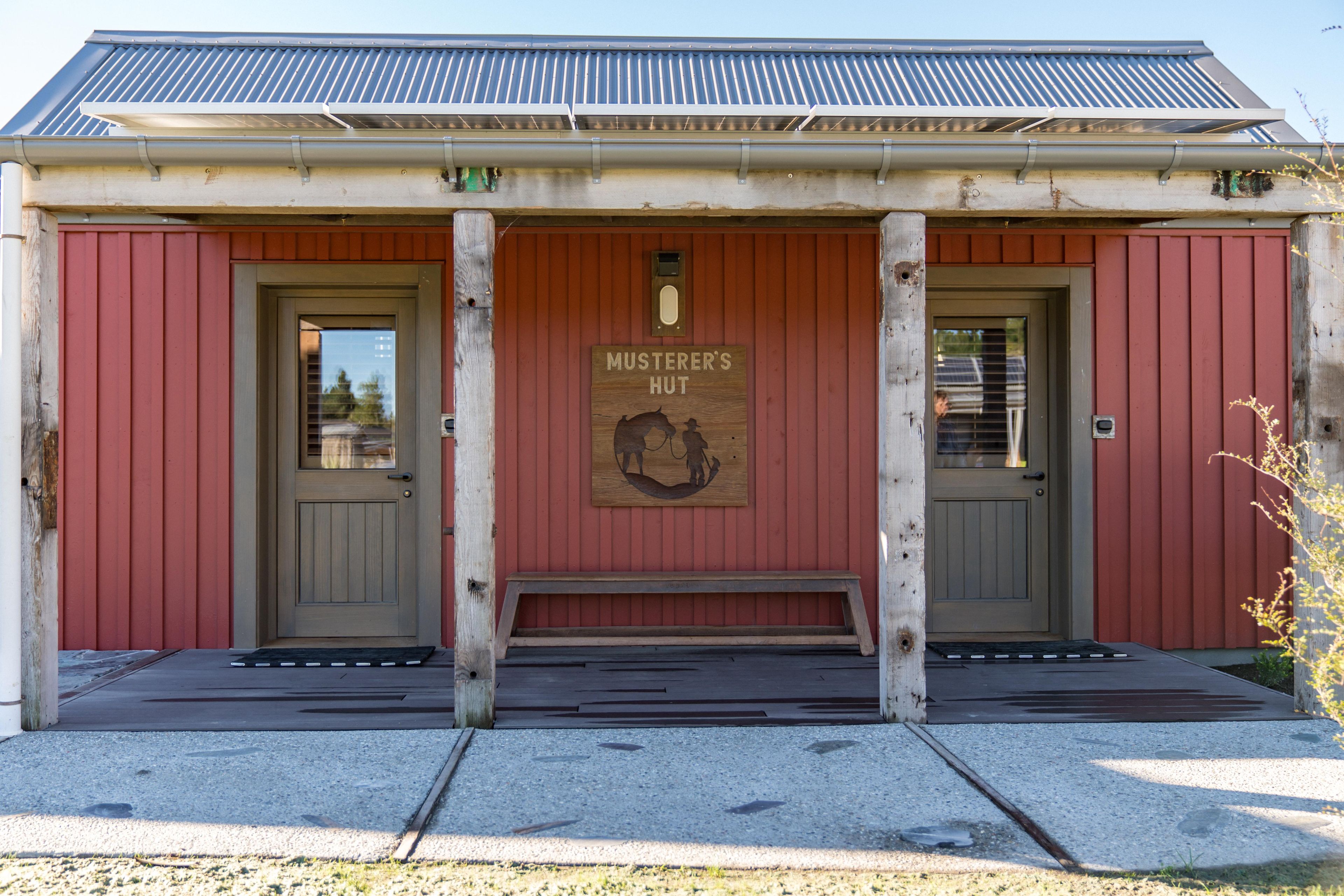Un bâtiment sur lequel est apposée une enseigne indiquant « MUSTERER’S HUT », et devant lequel se trouve un banc en bois.