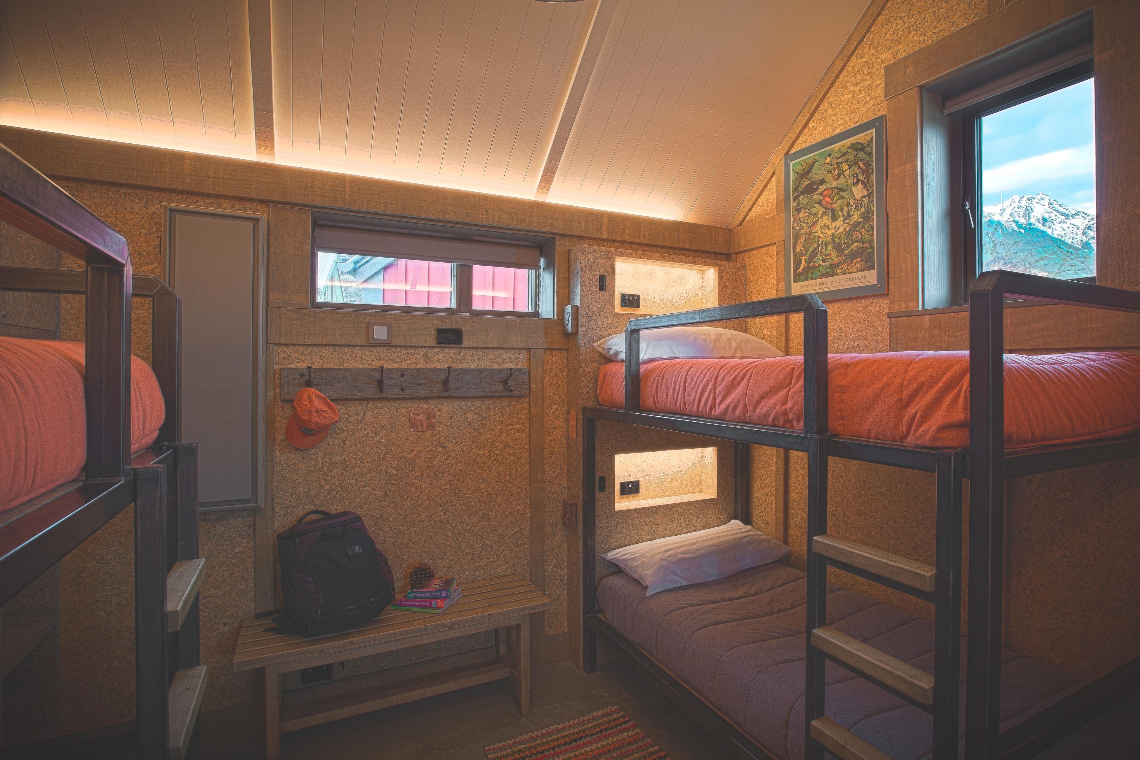 A bunk bed room with a window, a shelf with books, and a small table.