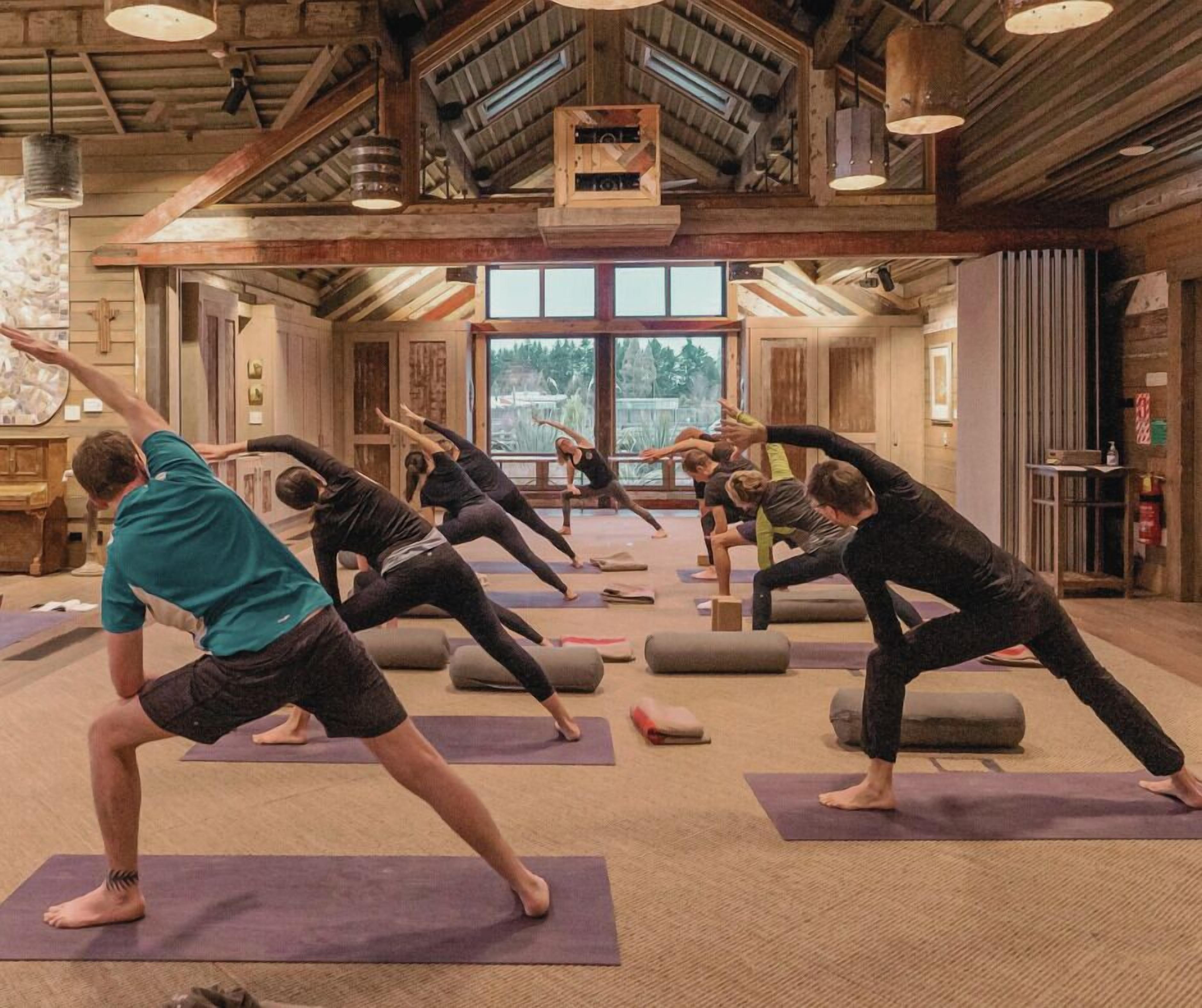 A yoga class in a rustic room with wooden beams and large windows.