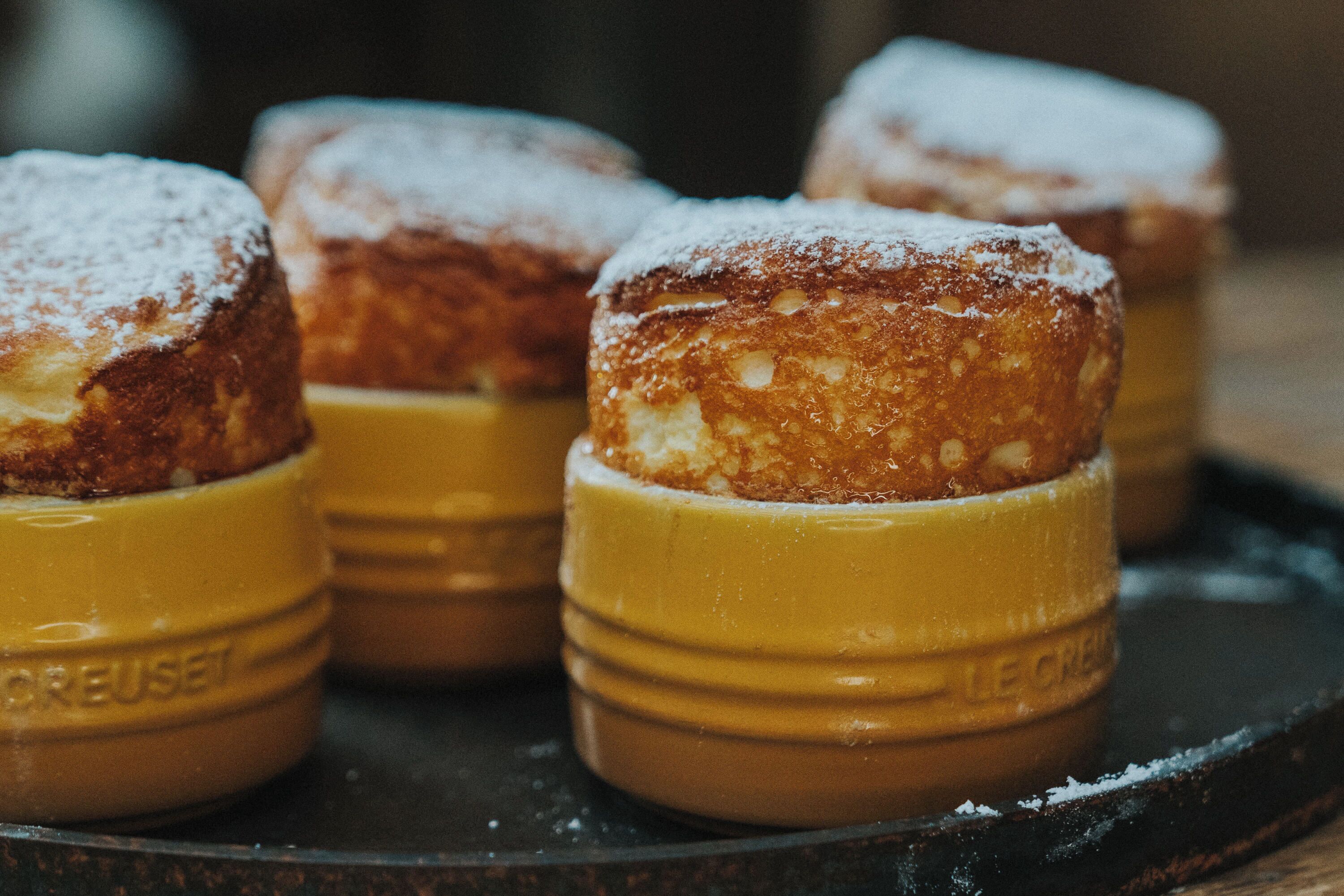 Cuatro pasteles en recipientes amarillos, espolvoreados con azúcar glas.