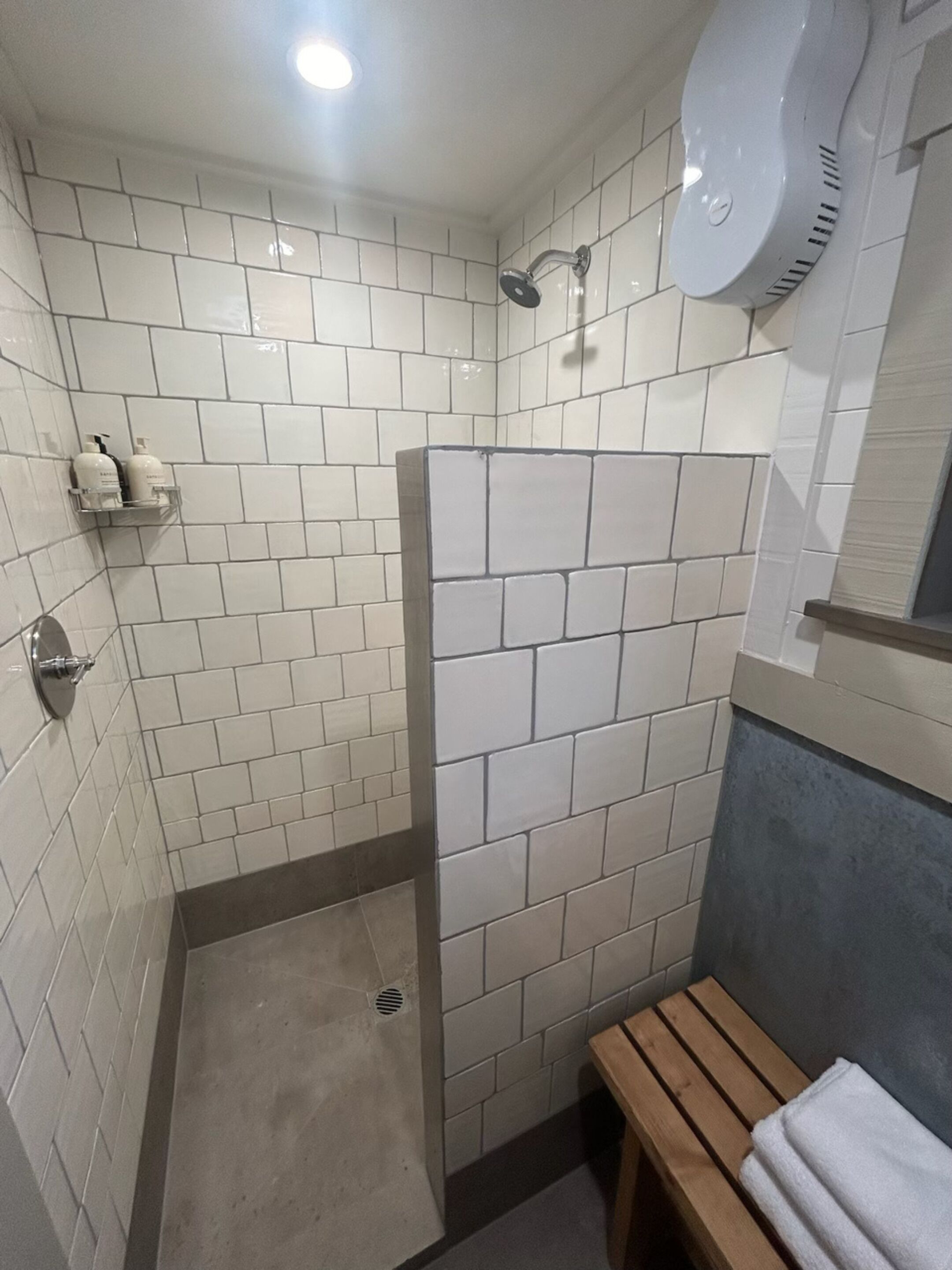 Um banheiro pequeno com azulejos, chuveiro, um banco e porta-toalhas.