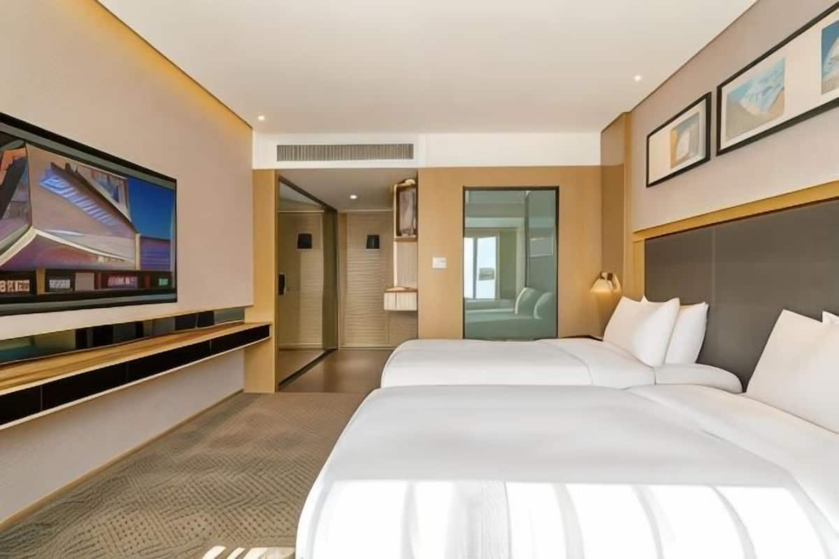 A hotel room with a TV, two beds, a desk, and a door leading to a bathroom.