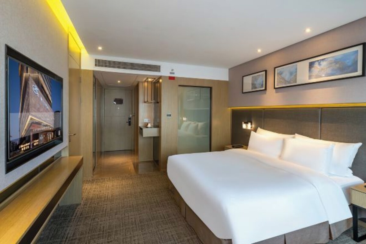 A hotel room with a large bed, a bedside table, a TV mounted on the wall, and framed pictures above the bed.