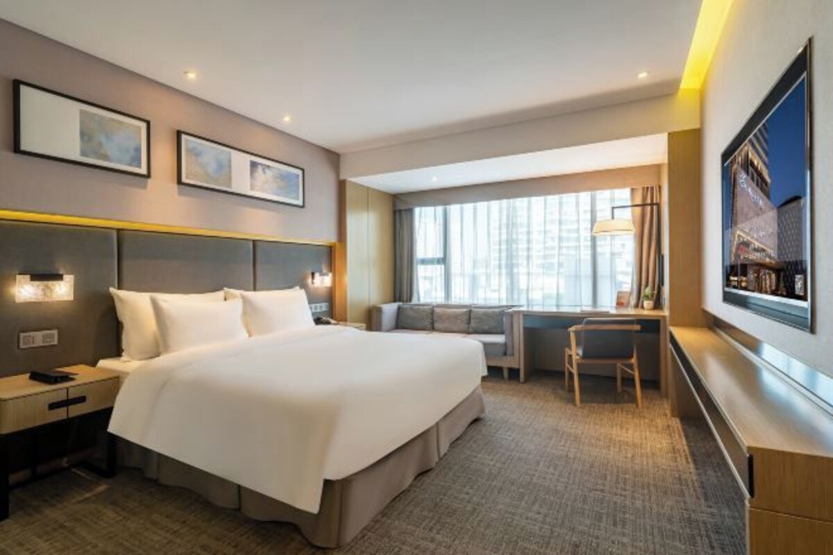 A hotel room with a large bed, a desk, a chair, and a window with curtains.