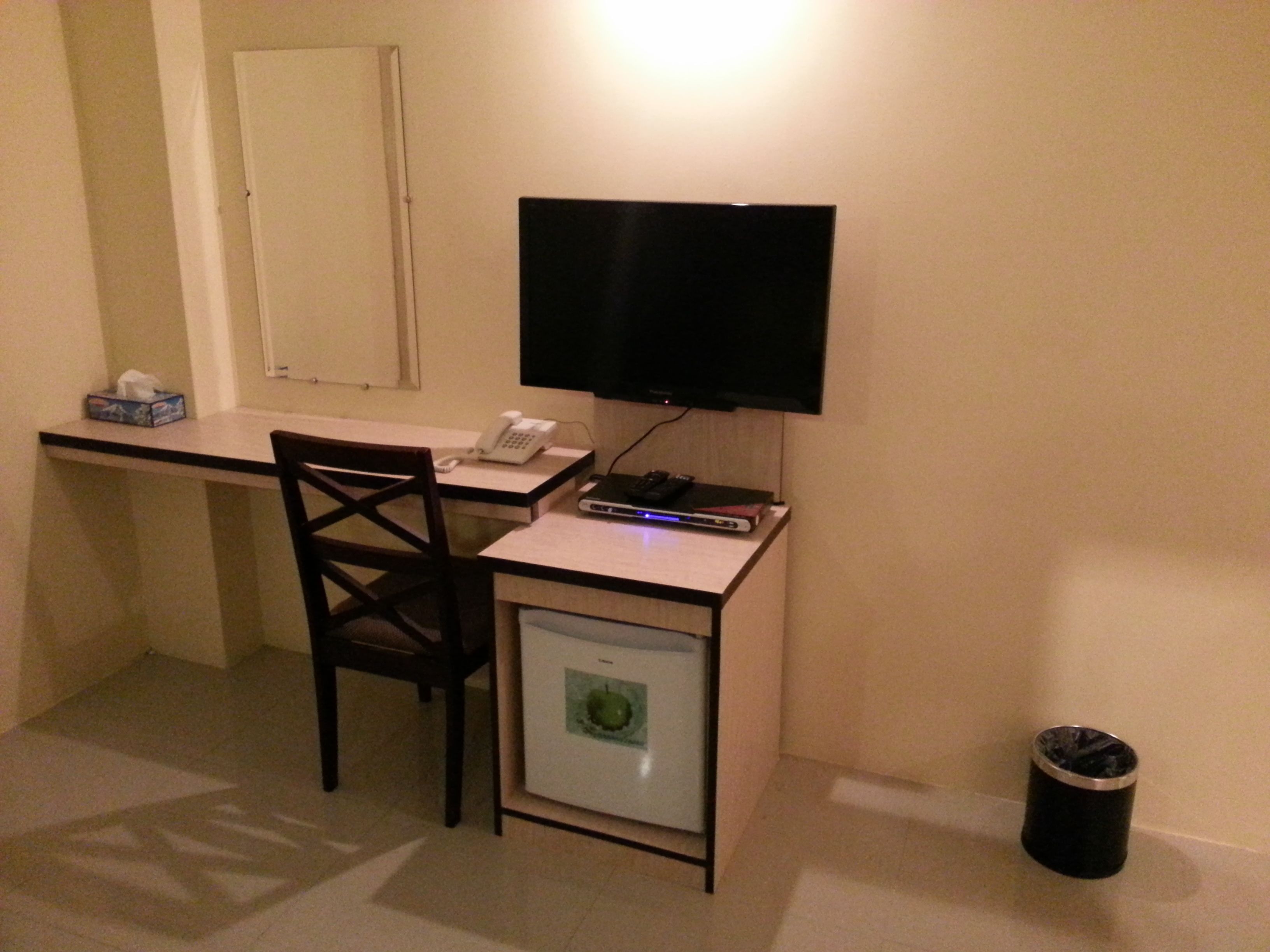 Ein gemütlicher Raum mit Schreibtisch, Stuhl, Fernseher und kleinem Kühlschrank.