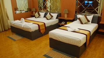 A hotel room with two beds, wooden flooring, a mirror, a TV, and a telephone on the nightstand.
