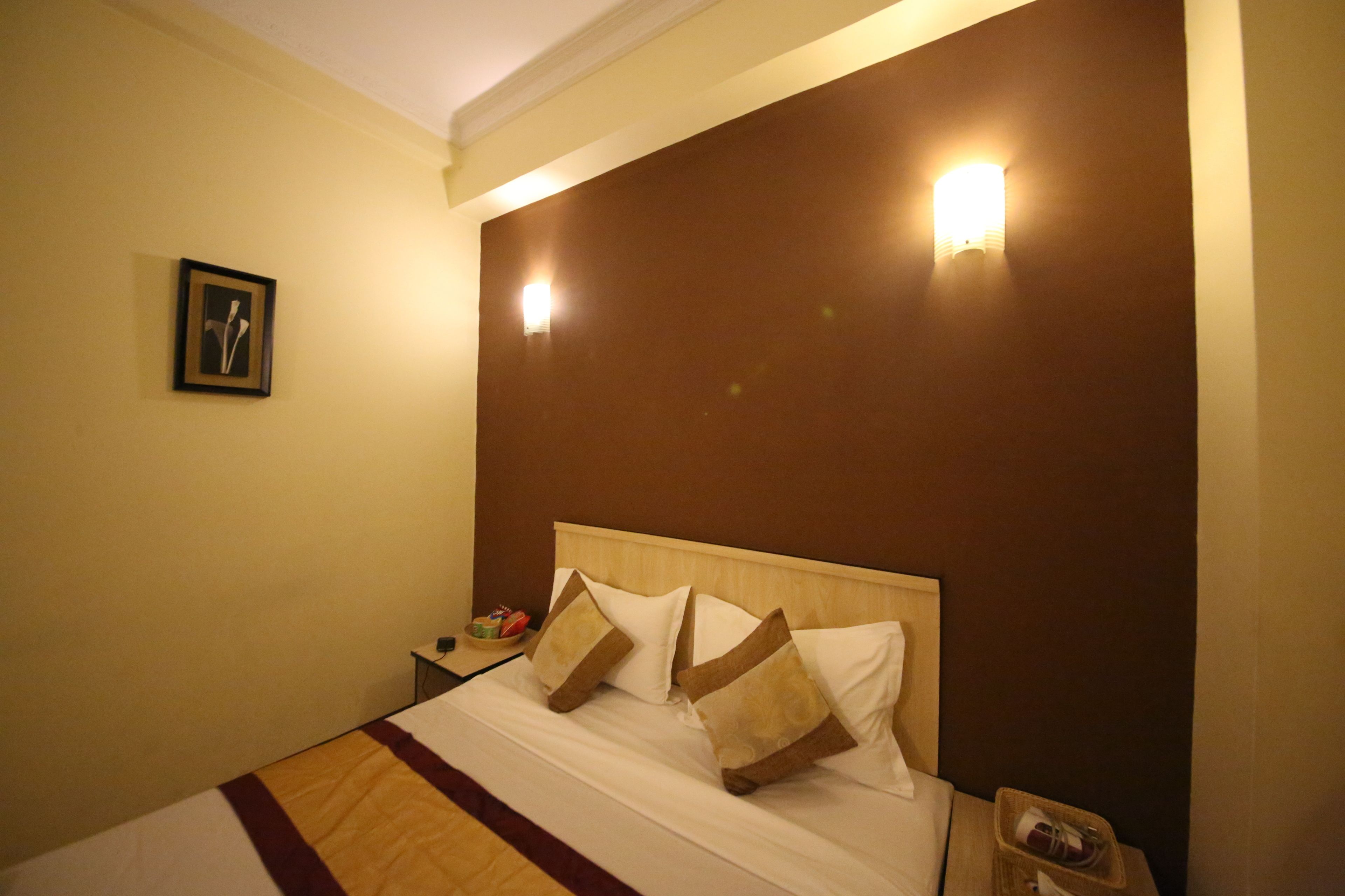 A hotel room with a bed, a nightstand, and a wall-mounted light fixture.