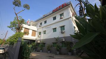 Un hotel con un letrero que dice 'PLATINUM HOTEL' y varios equipos de aire acondicionado. Hay plantas en macetas y un coche estacionado adelante.