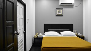 Habitación de hotel con cama, mesita de noche, aire acondicionado instalado en la pared, un cuadro enmarcado y una puerta.
