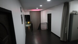 Un pasillo con escalera, una puerta y un ventanal con cortinas.