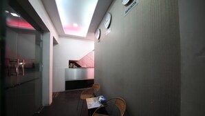 Un pasillo con sillas de mimbre, una recepción y relojes en la pared.