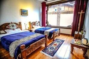 A room with two wooden beds, a large window with a view of a traditional building, a wooden table with a kettle, and a colorful rug. - Energy Healing Space Inn (Deqin)