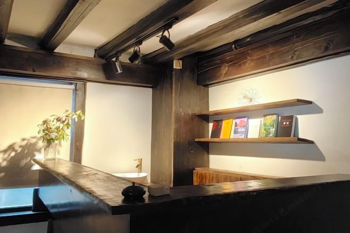 A modern bathroom with a wooden vanity, a white sink, and a shelf with books.