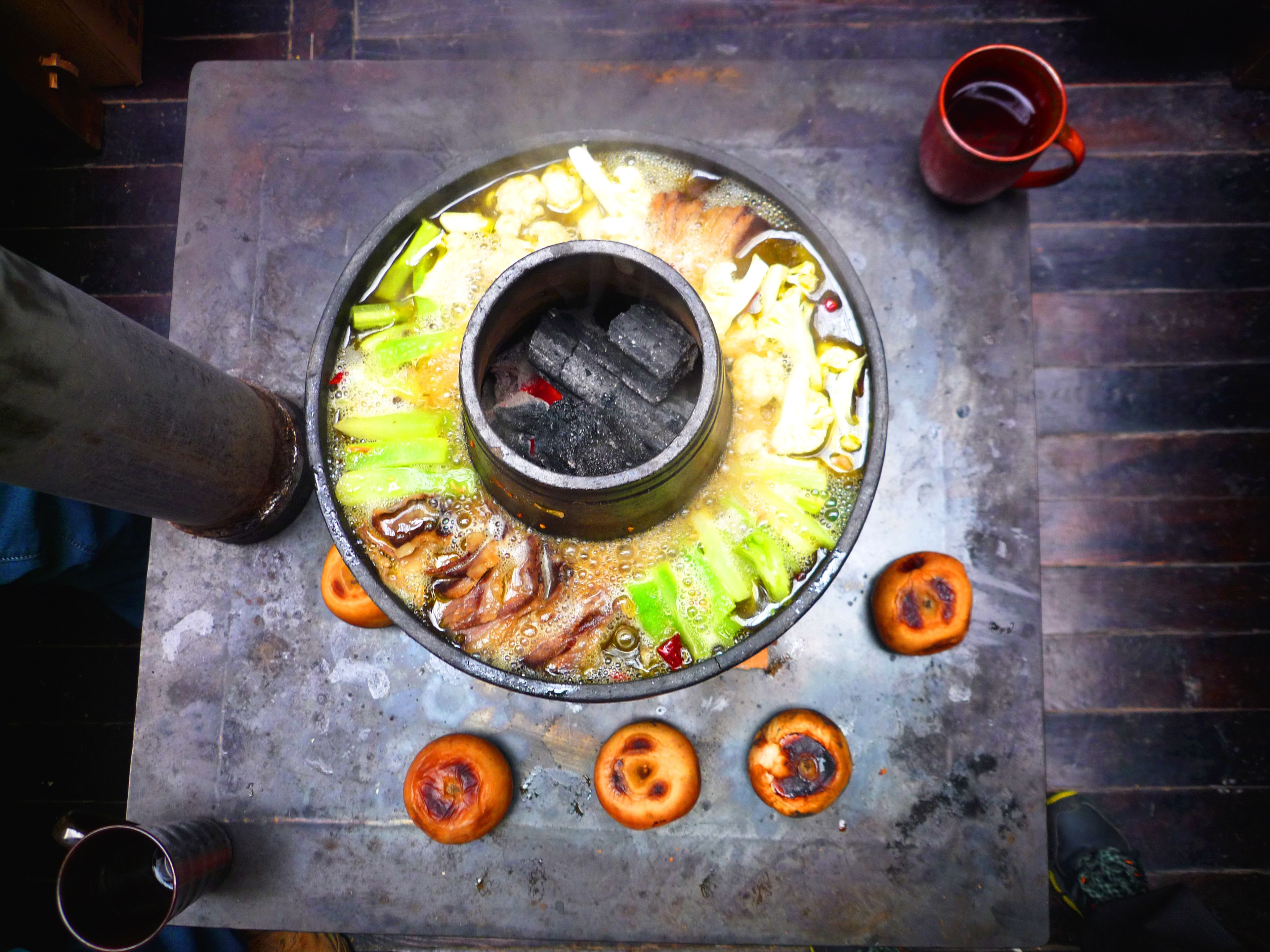 A hot pot setup with vegetables and meat, a metal table, and a red cup.