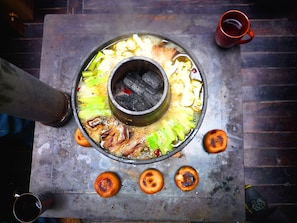 A hot pot setup with vegetables and meat, a metal table, and a red cup. - Energy Healing Space Inn (Deqin)