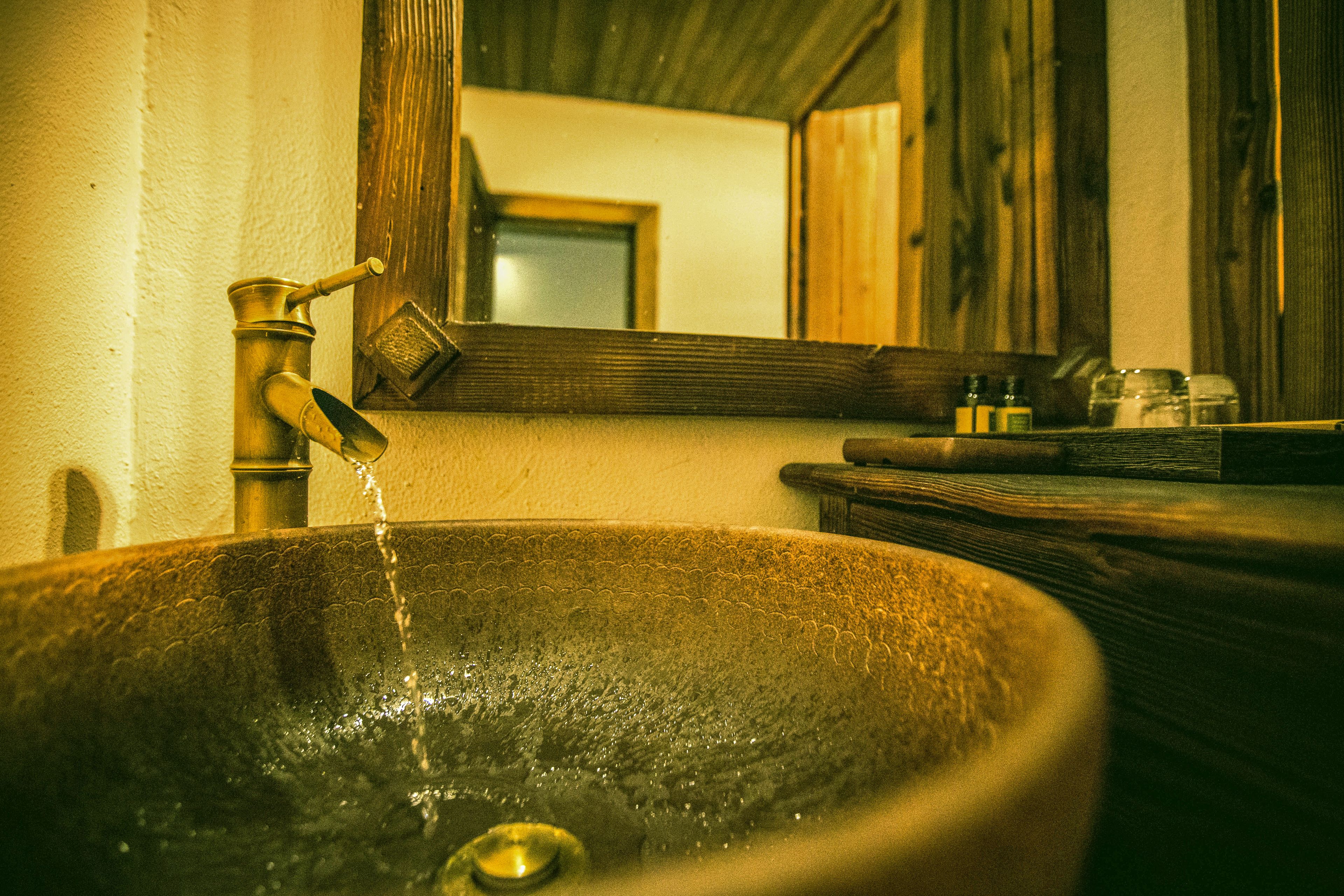 A large, rustic stone sink with running water, a wooden countertop, and a mirror reflecting a door and wall.