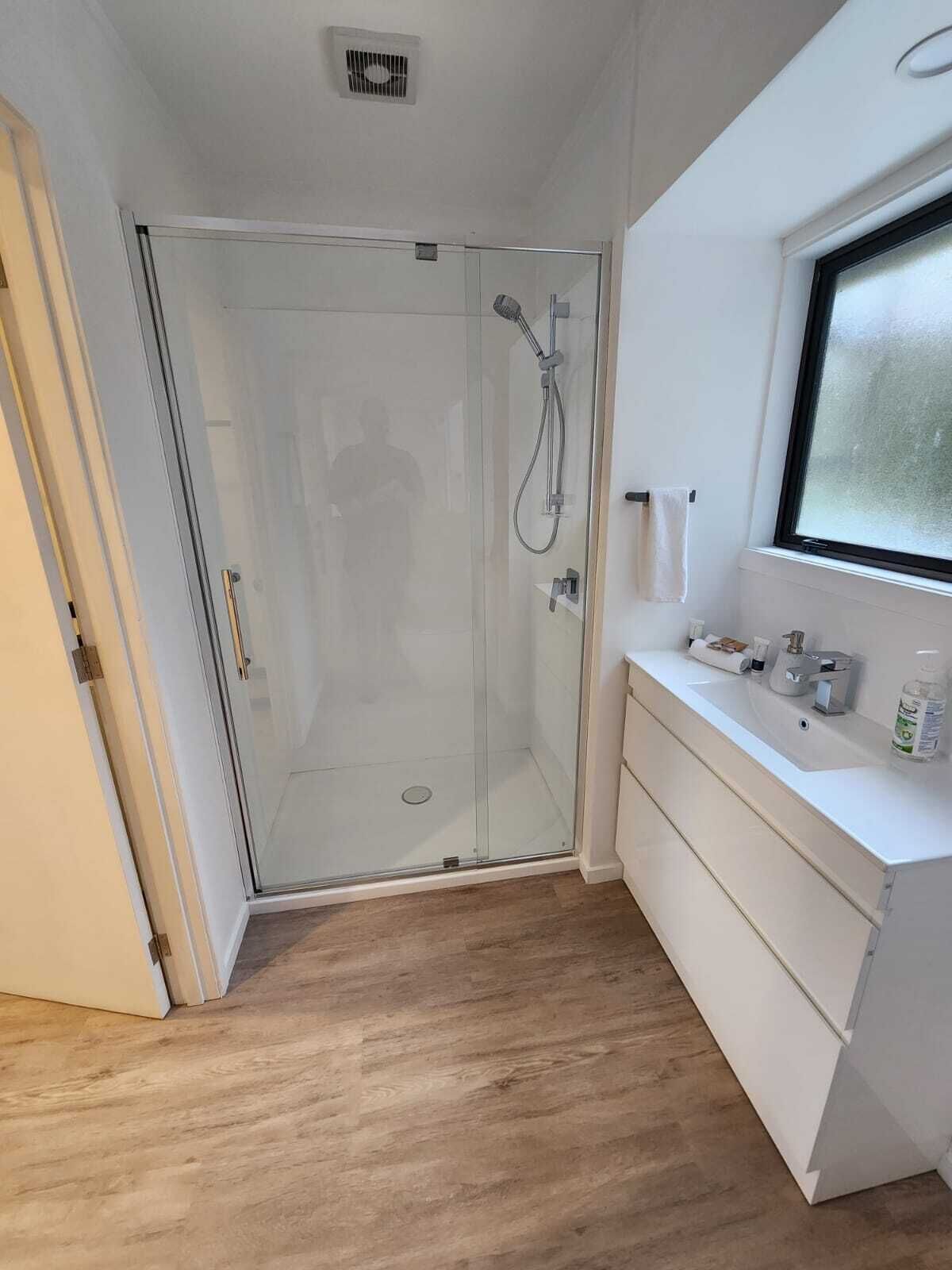 A modern bathroom with a glass shower enclosure, a white vanity with a mirror, and a window.