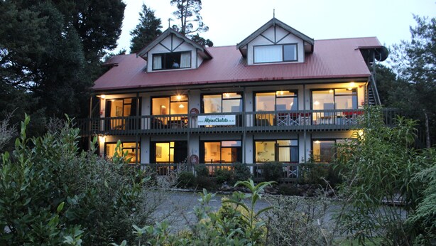 En bygning med flere etager, rødt tag, balkoner og et skilt, der angiver, at det er en alpechalet.