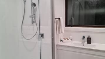 A modern bathroom with a glass shower enclosure, a white sink with toiletries, and a large window.