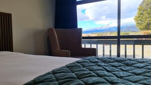 Et hotelværelse med seng, stol og balkon med udsigt til et bjerg.