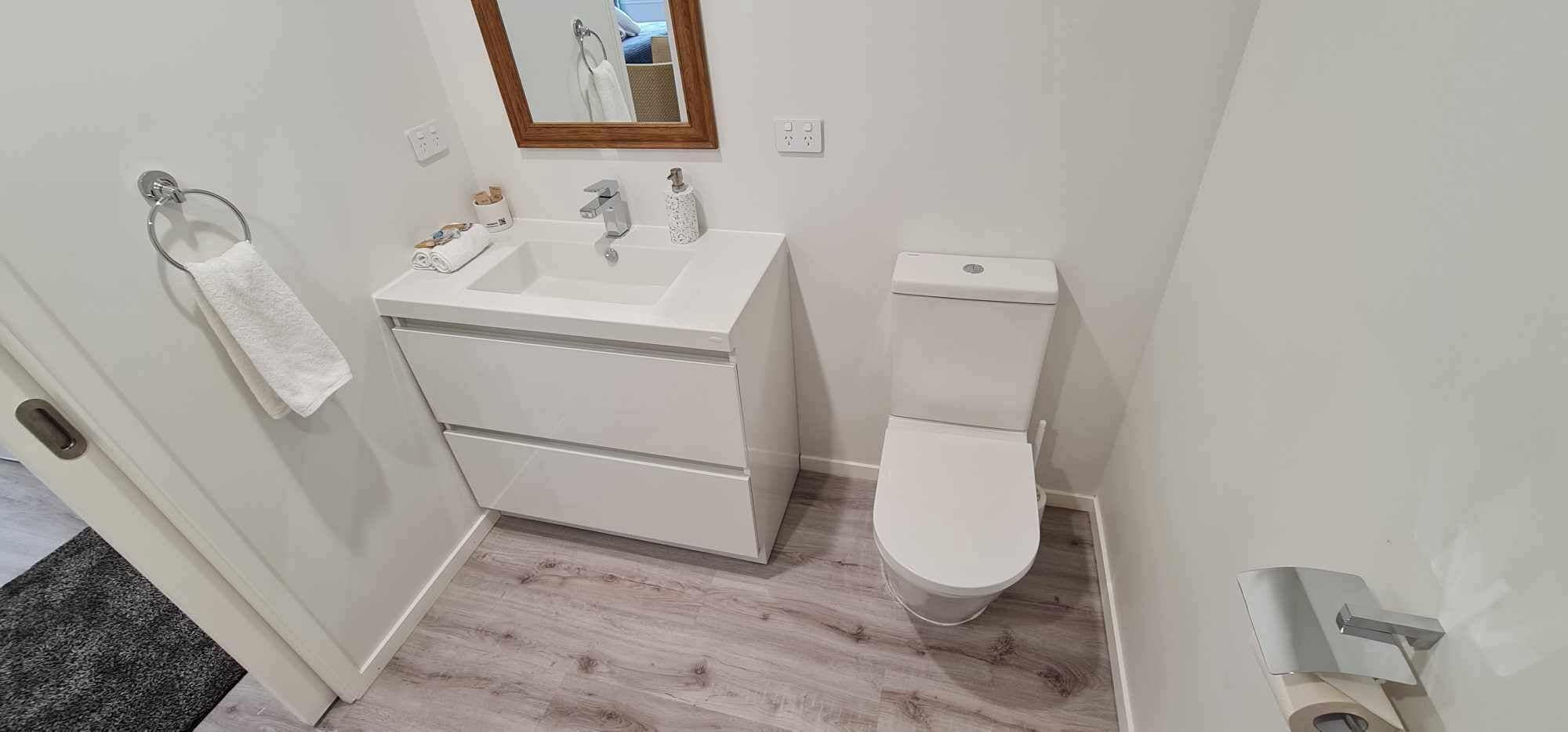 A small, modern bathroom with a white sink, toilet, and mirror.
