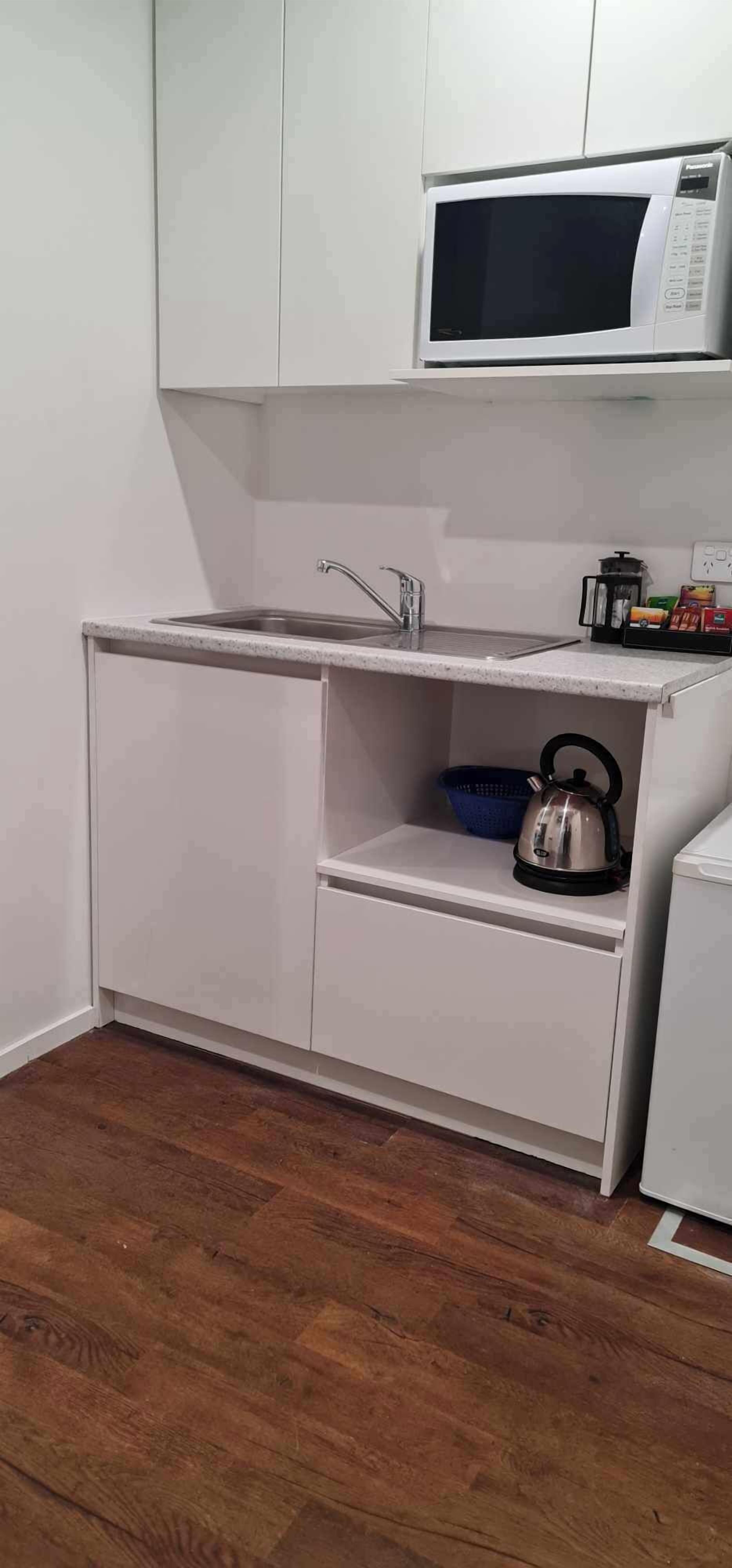 A compact kitchen with a microwave, sink, and a kettle on a shelf.